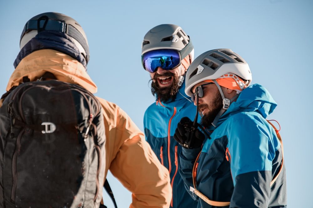 Trije smučarski alpinisti v čeladah, z očali in nahrbtnikom