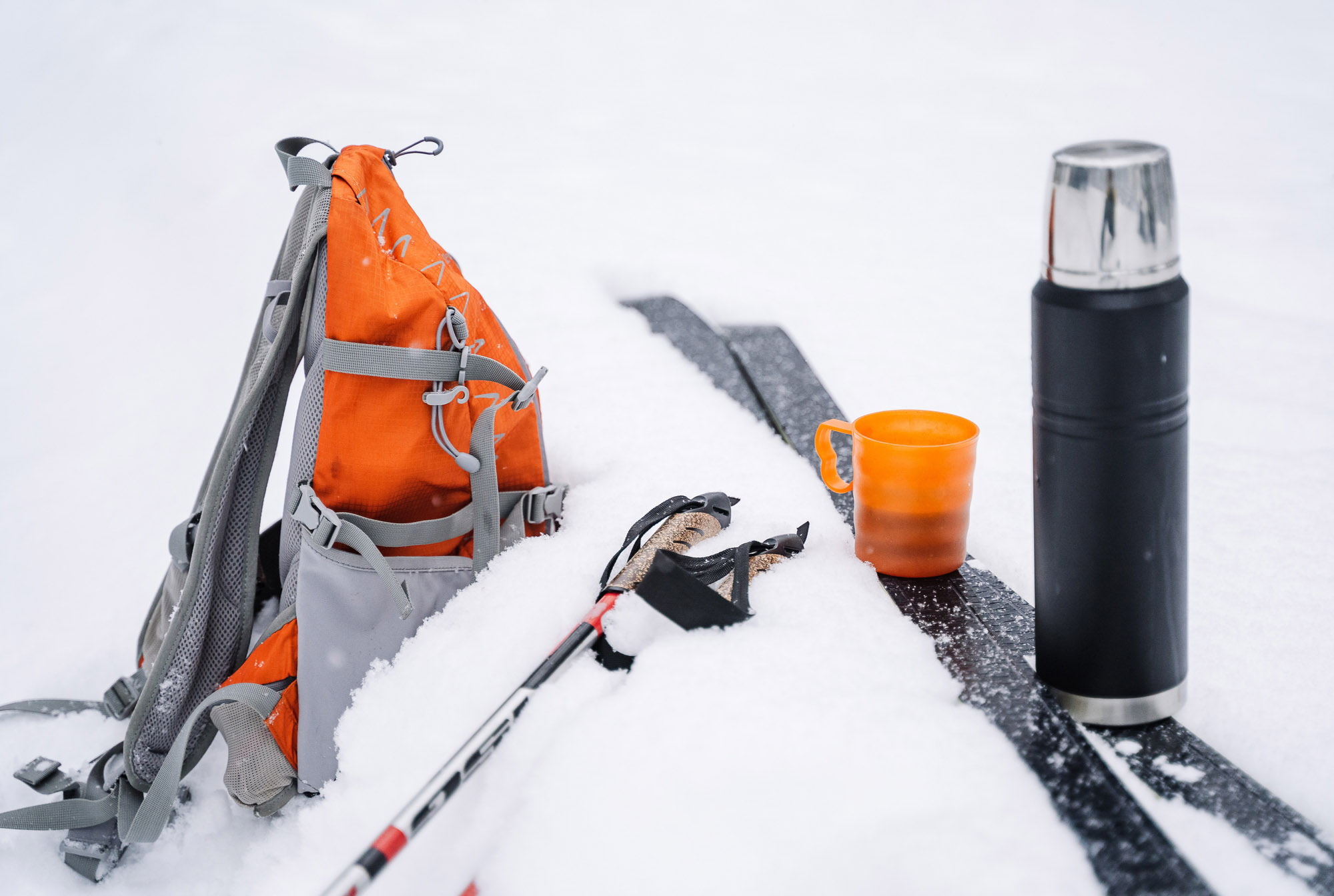Rucksack im Schnee und Thermoskanne auf den Skiern