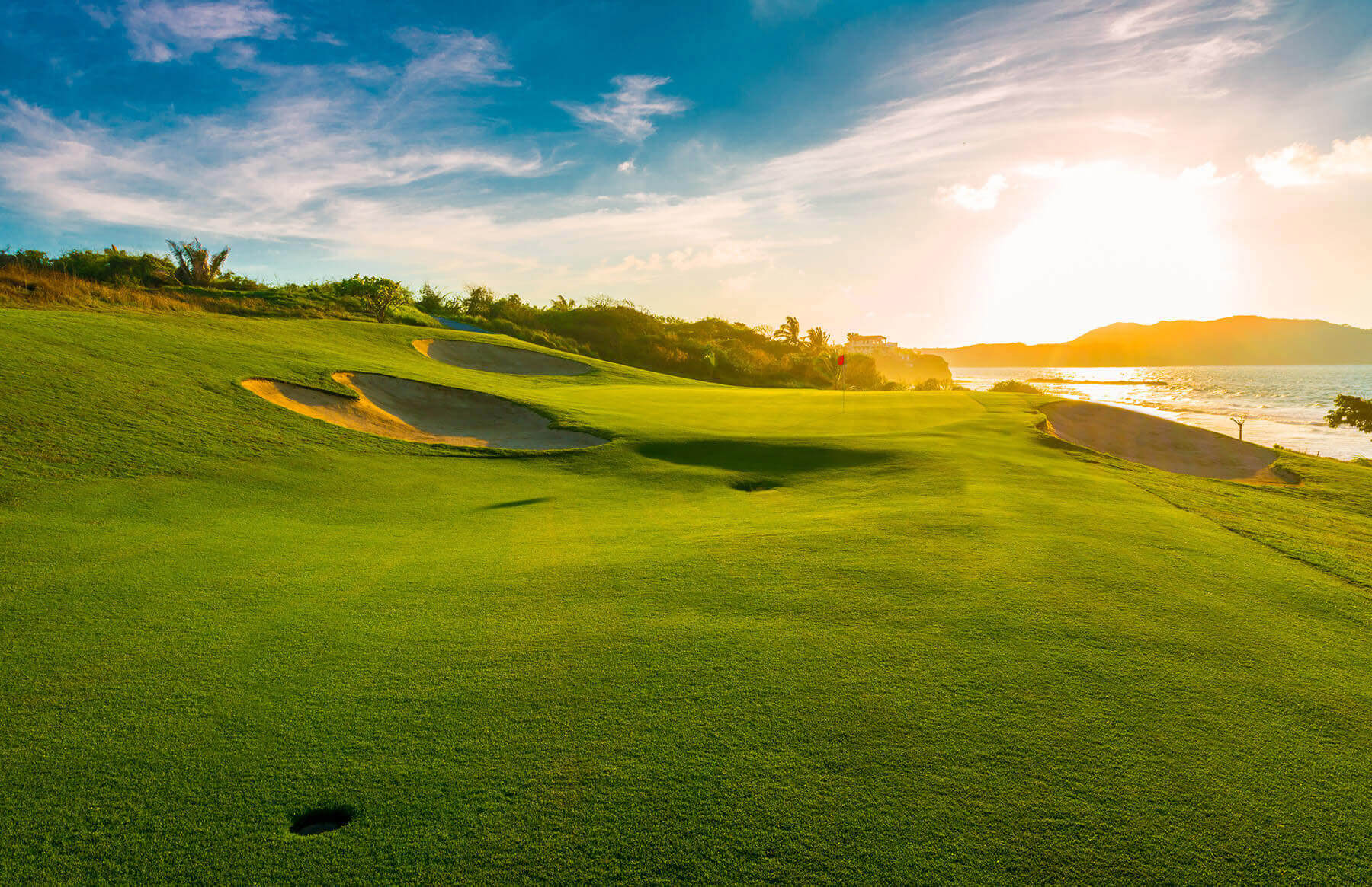 Scenérie golfového hřiště s bunkry při západu slunce u moře