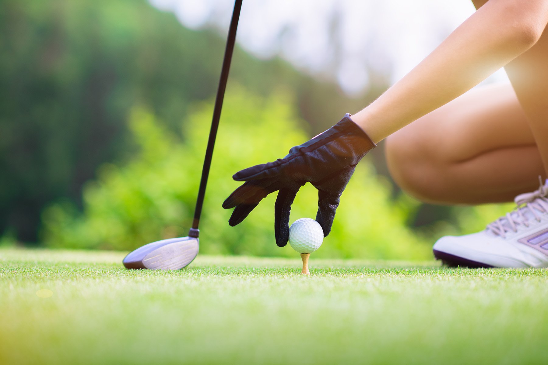A female hand wearing a glove places a golf ball on a tee