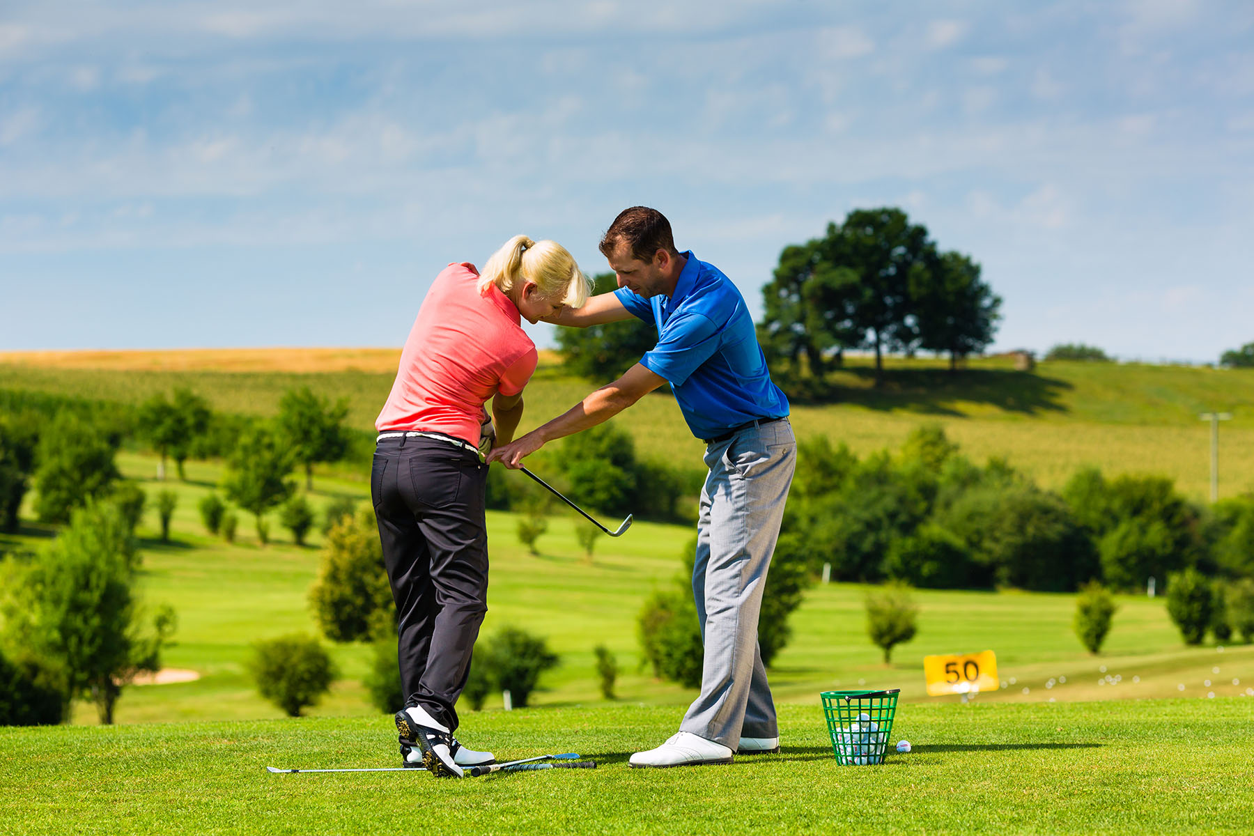 A woman learning to play golf with a trainer on a golf course