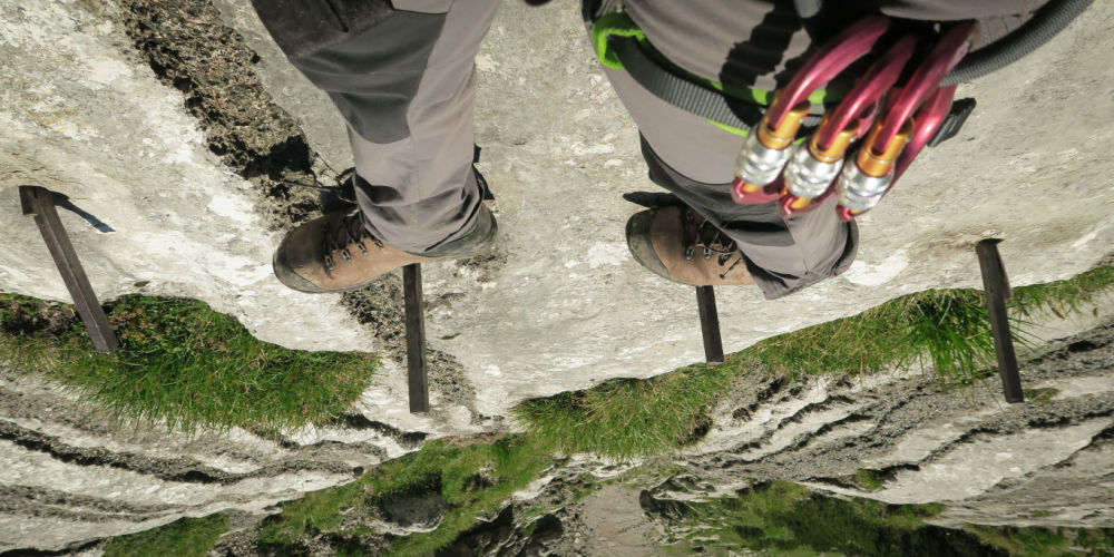 View of the climber's feet on the via ferrata and the depth below